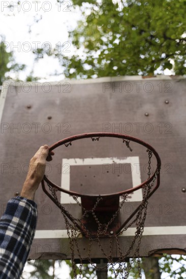 A hand reaches up to grab an old, iron basketball hoop with a chain net in an outdoor area