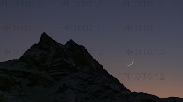 The crescent Moon gracefully hangs over the silhouette of the Dents du Midi mountain in the Swiss