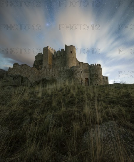 Majestic night view of Manqueospese Castle in Avila, Spain, with starry sky backdrop and wispy