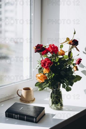 A serene windowsill featuring a bouquet of vibrant roses in a glass vase, a Bible, and a warm-toned