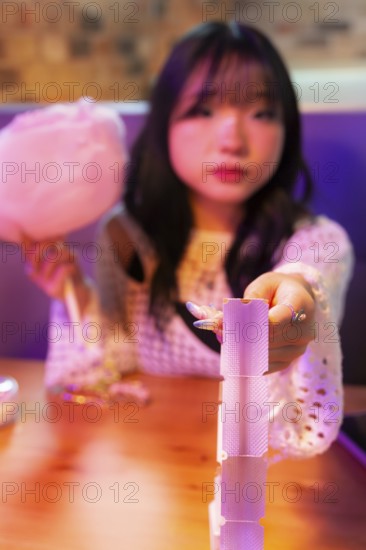 An Asian Gen Z girl delights in the arcade atmosphere, holding cotton candy while playing a game