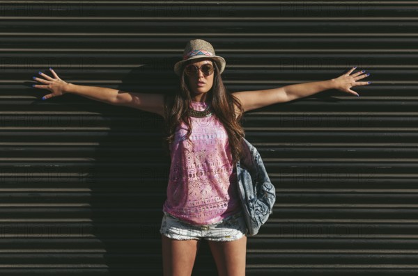 A fashionable woman poses confidently against a dark background, wearing a pink sleeveless top,