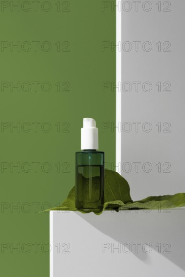 Close-up view of a green glass essential oil bottle placed on a white stand with a large green
