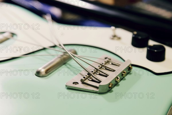 Close-up of a bass guitar bridge and strings in a luthier workshop. The focus is on the intricate
