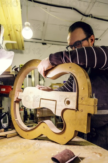 A skilled luthier at work in a workshop, carefully crafting a bass guitar using specialized tools