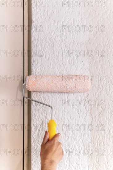 Cropped unrecognizable of a man's hand using a paint roller on a textured wall, capturing a moment