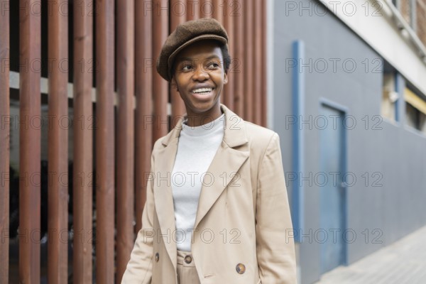 A black woman in an urban environment, wearing a stylish beige outfit paired with a beret She