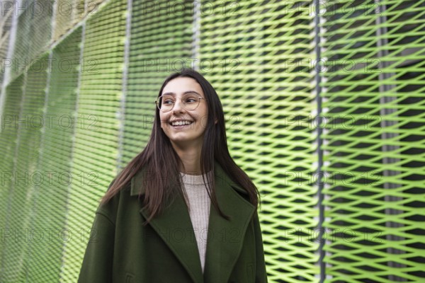 A woman in a stylish green coat smiles joyfully while standing against a vibrant, abstract green