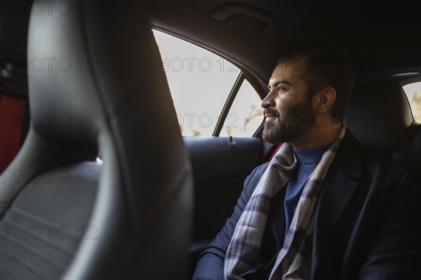 Indian male businessman dressed in formal wear with a winter scarf, traveling in the backseat of a