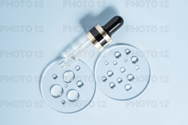 A pipette dropper with a skincare serum rests on a smooth, light blue surface Surrounding the