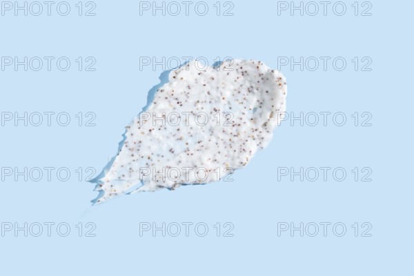 Exfoliating cream with microbeads smeared against a pale blue background, showcasing the texture