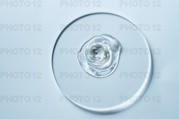 A clear gel with small golden specks on a round glass plate against a light blue background The