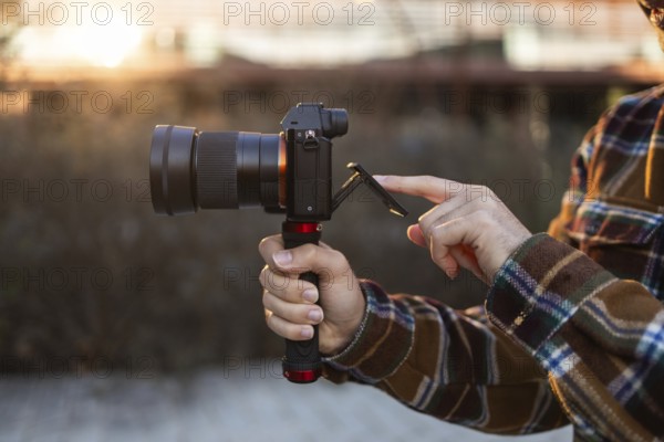 Close-up of hands holding a camera and adjusting the screen during golden hour The scene captures