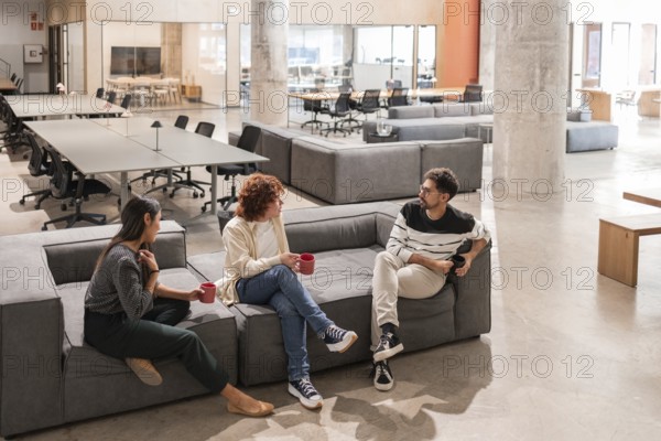 Three coworkers engage in a friendly and productive discussion in a modern office lounge,