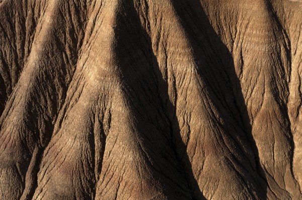 Aerial view of a rugged desert landscape showcasing intricate erosion patterns and ridges in brown