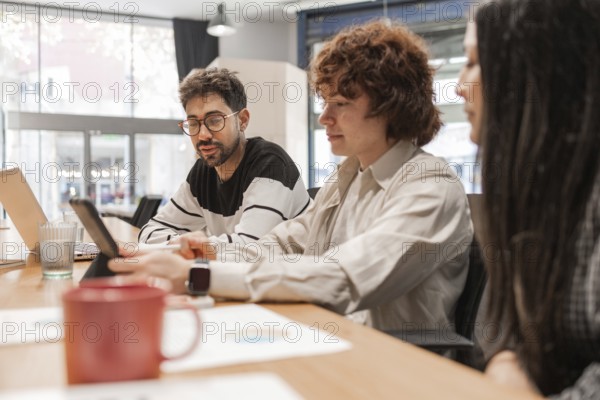 Three coworkers discuss projects around a wooden table in a bright, modern office They share ideas