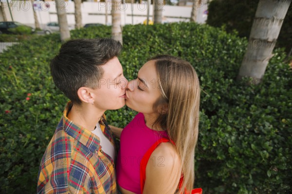 Happy lesbian couple sharing a kiss in a lush outdoor setting, celebrating love and diversity.