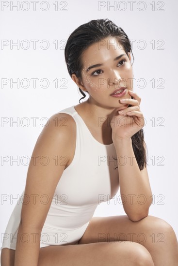 A fresh portrait of a young woman wearing a white bodysuit in a studio setting, gazing slightly