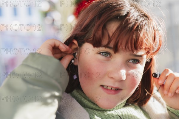 A girl with auburn hair adjusts her earbud while seated on a bus, showcasing a moment of technology