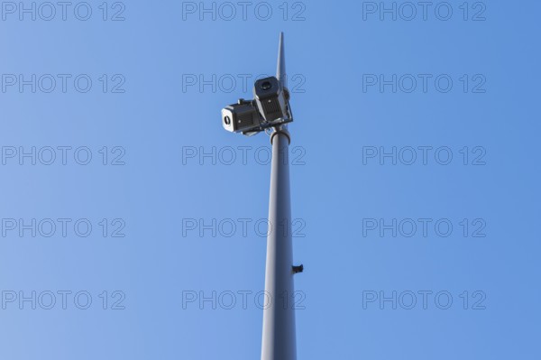 Low-angle view of surveillance cameras mounted on a tall pole, set against a clear blue sky. The