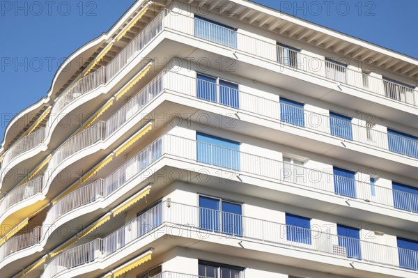 A modern apartment building features multiple curved balconies, white facade, and glass railings,