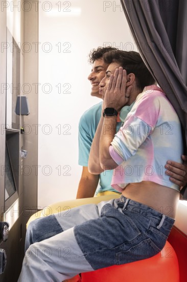 A joyful gay couple sits closely in a booth, sharing laughter and intimate expressions. They are