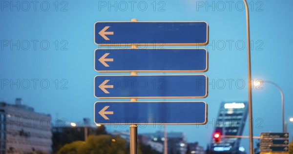 A street sign with multiple arrows pointing to the left, set against a cityscape. The scene