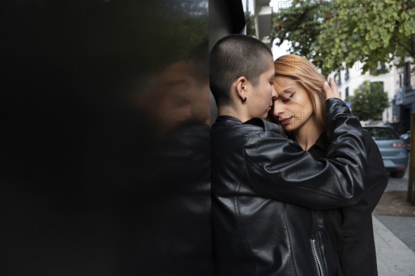 A loving lesbian couple shares an intimate, tender moment while standing closely against a wall in