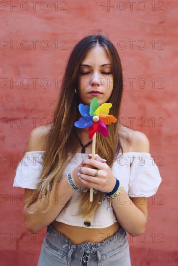 A teenage girl with long hair holds a vibrant pinwheel against a coral backdrop. She appears calm