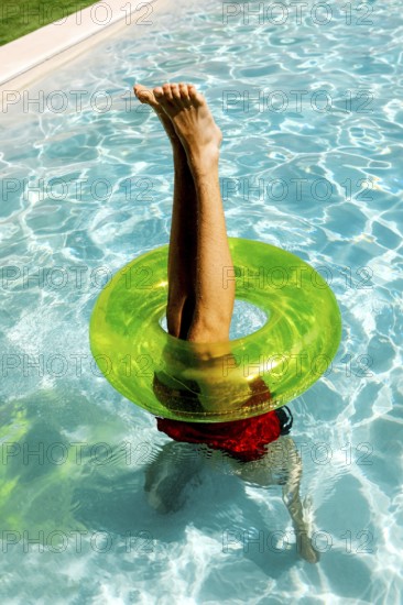 A person playfully balances upside down in a swimming pool, legs pointing skyward through a bright