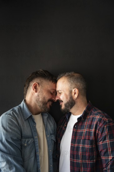 A happy gay couple shares a tender moment, leaning forehead to forehead. Their connection is