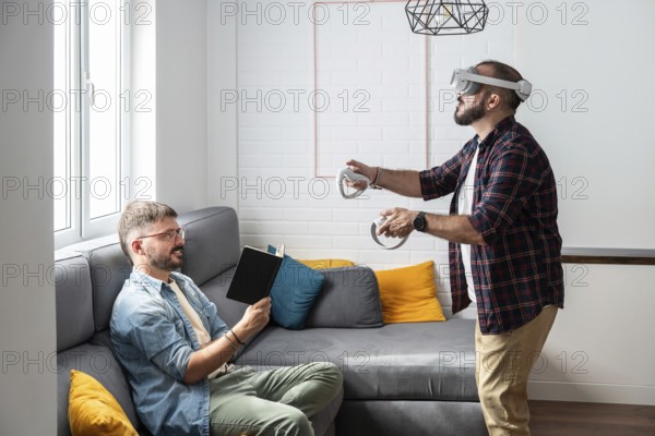 A gay couple engages in leisure activities in their living room. One reads a book while the other