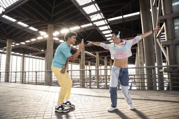 A lively gay couple enjoys a playful moment in an urban setting. One person, wearing colorful