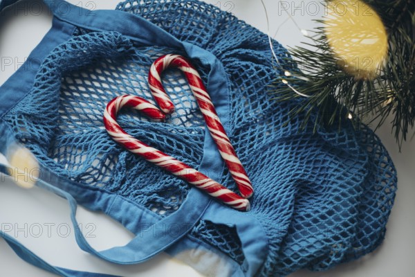 A vibrant blue string bag lays on a white surface, gently cradling two candy canes formed into a