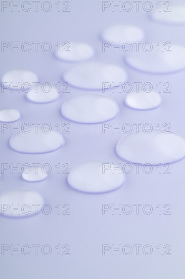 Close-up image of droplets scattered on a smooth, lavender-colored surface The droplets vary in