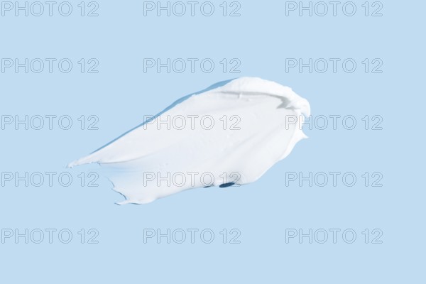 Smooth texture of a white cream or gel smear, isolated on a serene blue background, representing
