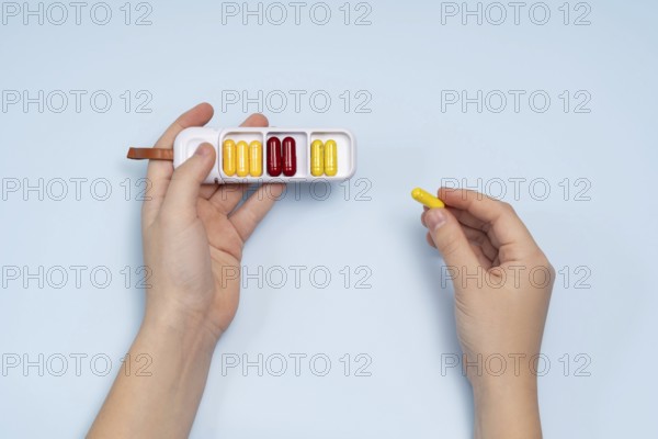Top view of a cropped unrecognizable person's hand holding a white pill box filled with colorful