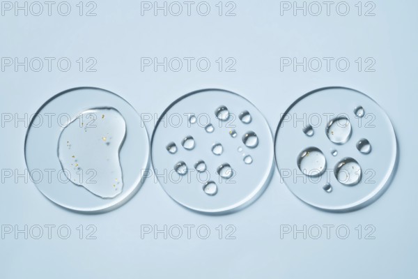 Three transparent petri dishes with water droplets placed on a light blue surface The circular