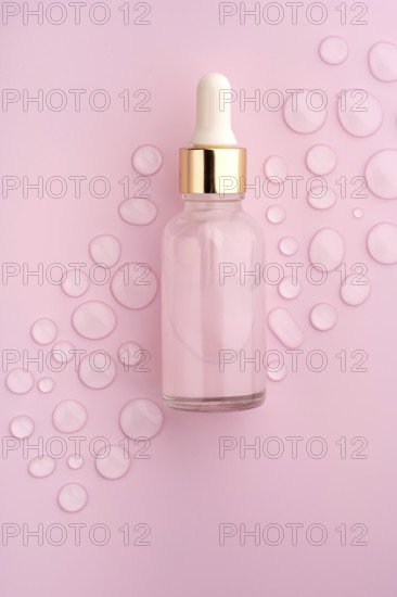 A clear glass dropper bottle on a pink background, surrounded by scattered water drops The scene