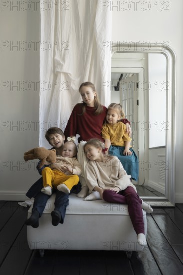 Five children, dressed in vibrant outfits, sit and play together in a cozy room with a large mirror