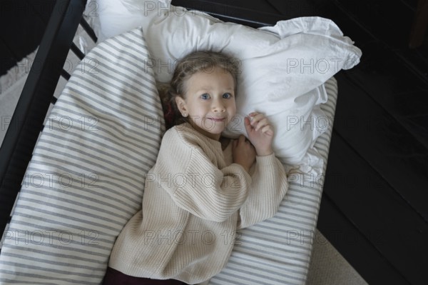 A child with light hair and blue eyes lies comfortably in bed, wearing a cozy sweater The bed is