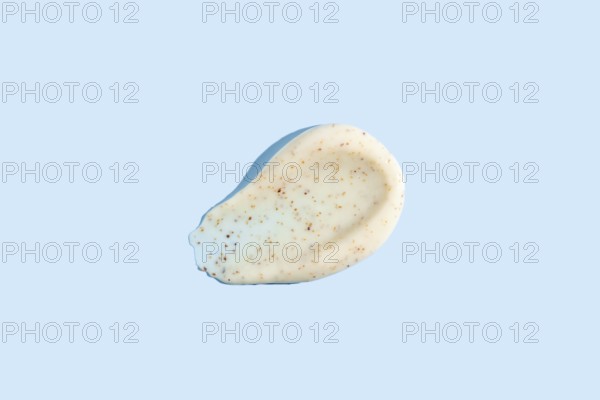 A dab of exfoliating cream with visible scrub particles smeared on a pastel blue background