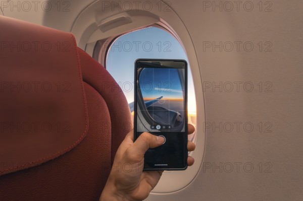 Cropped unrecognizable person captures a sunset over the ocean using a smartphone, viewed through
