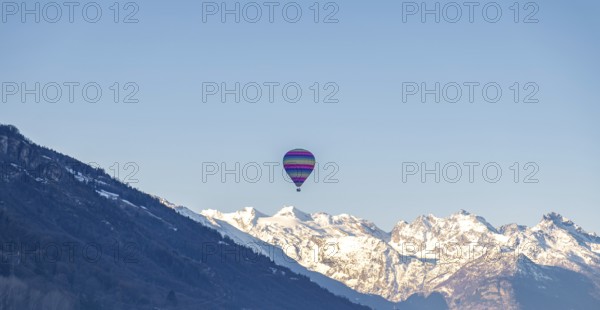 A vibrant hot air balloon floats gracefully over the Swiss Alps, showcasing a panorama of snow-clad