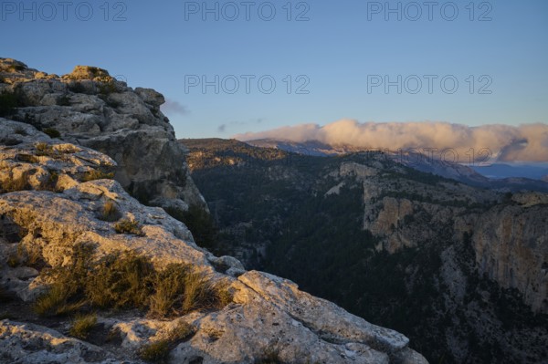 A stunning landscape of rocky cliffs and forested valleys illuminated by the warm light of sunset,