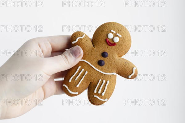 Close-up of a hand holding a cheerful gingerbread man cookie decorated with white icing The
