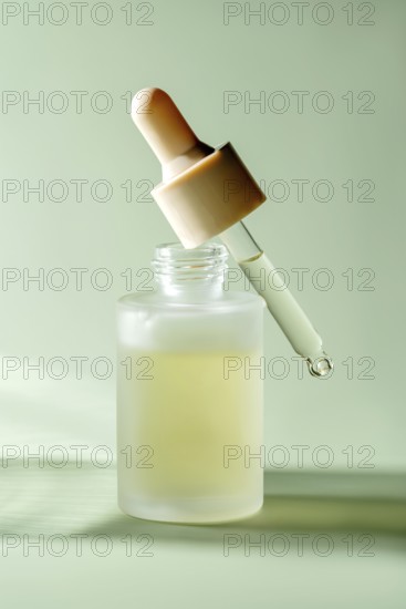 A translucent serum dropper bottle with a single drop hanging from the pipette, showcased against a