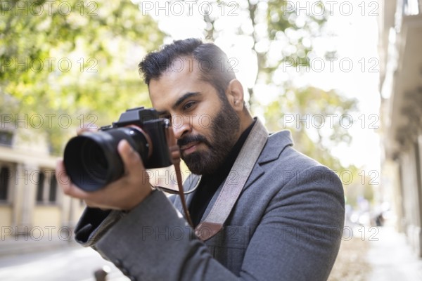 An Indian man, dressed professionally in a grey coat, focuses intently on capturing a photo with