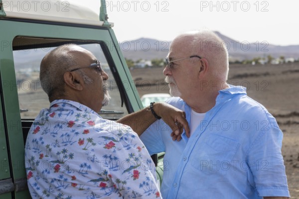 A senior gay couple shares a tender moment beside their off-road vehicle during a camping trip.