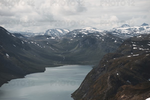A sweeping view of a tranquil lake nestled in a dramatic mountain valley in Norway Snow-dusted